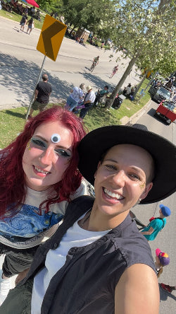 Two people taking a selfie on a street with a traffic sign and pedestrians in the background.