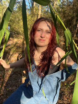 Picture of Artist - Person with red hair standing among tall green plants outdoors