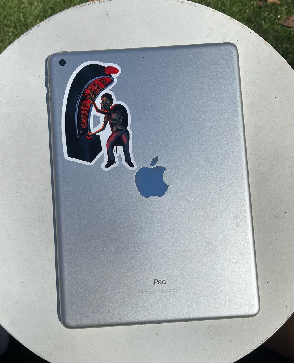 Sticker of a zombie playing a slot machine on an iPad on a white table outside