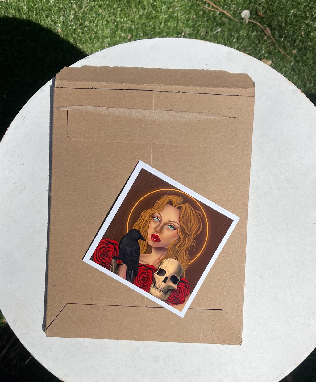 Cardboard envelope with a printed sticker of a woman with a bird and skull on a white surface.